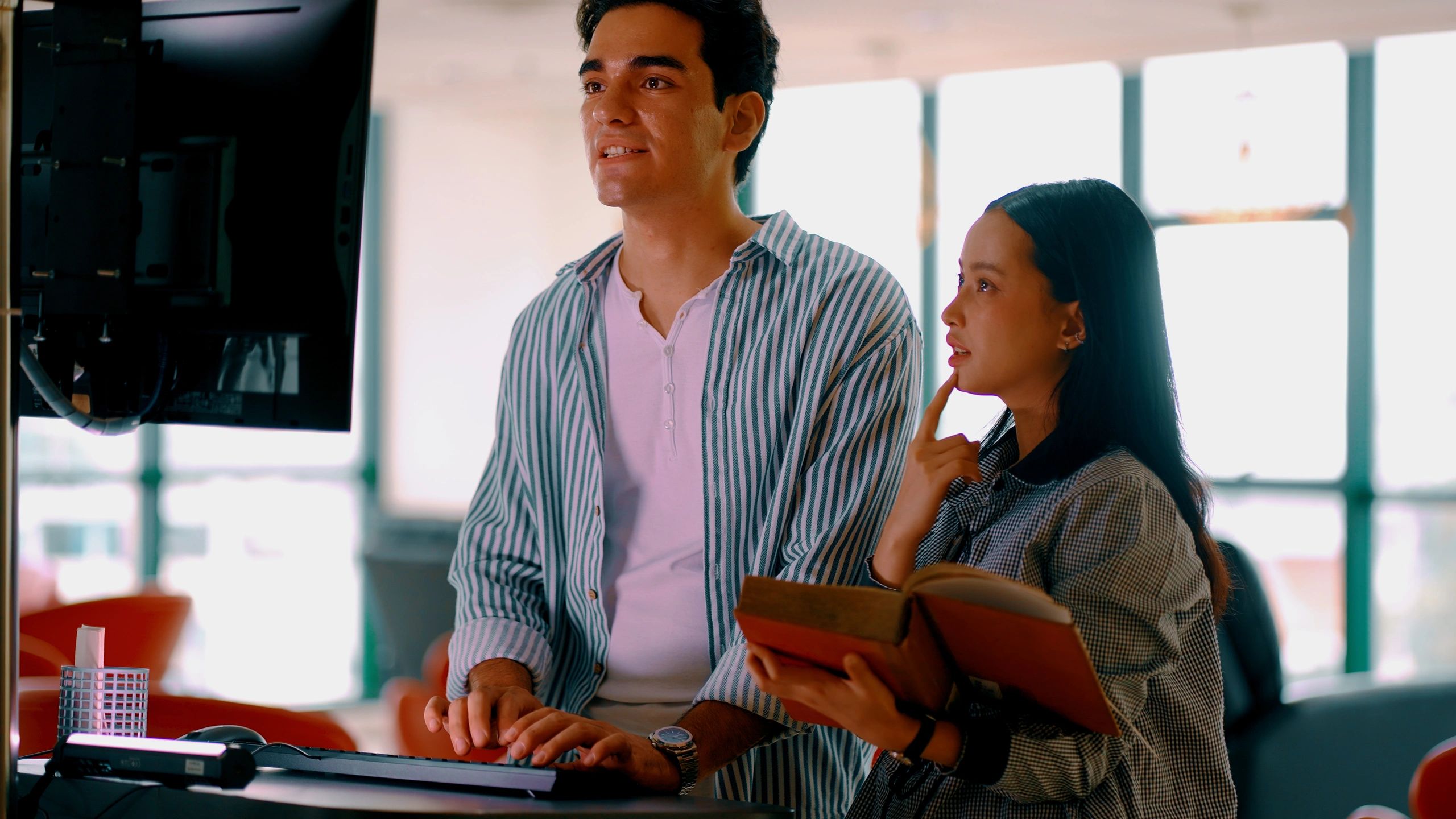 Two people collaborating at a computer in a bright workspace